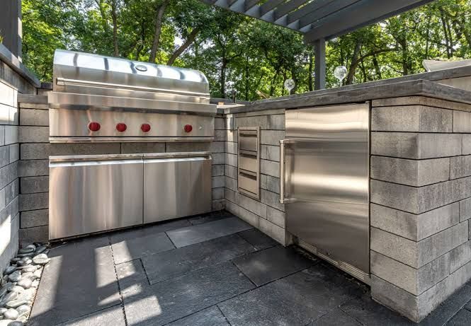 Stainless steel grill on a stone countertop with trees in the background, set on a patio.