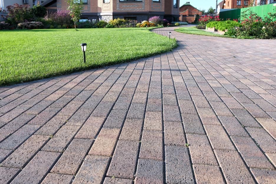 Brick walkway curves through a well-manicured lawn towards a house.