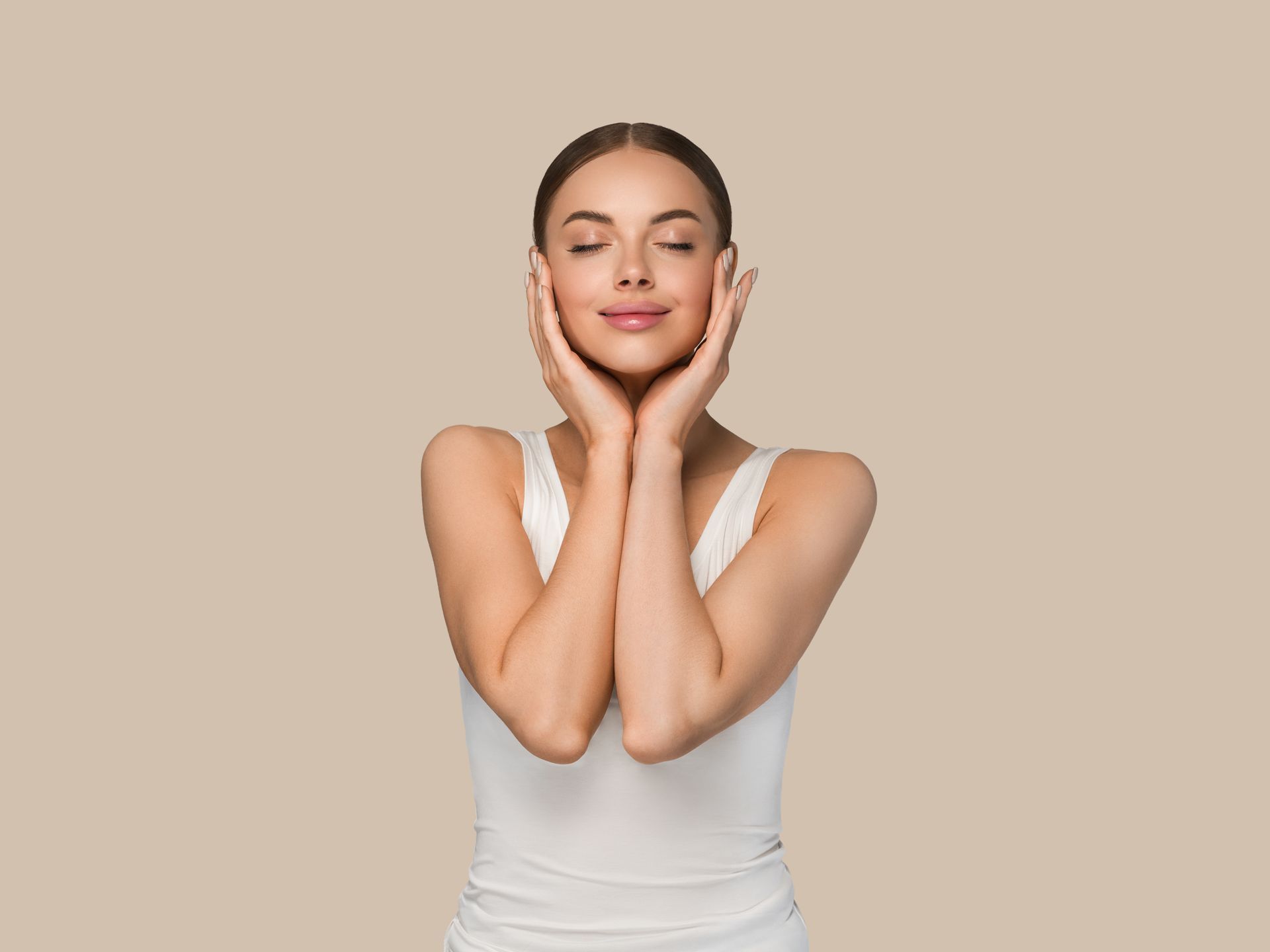 A woman in a white tank top is holding her hands to her face.