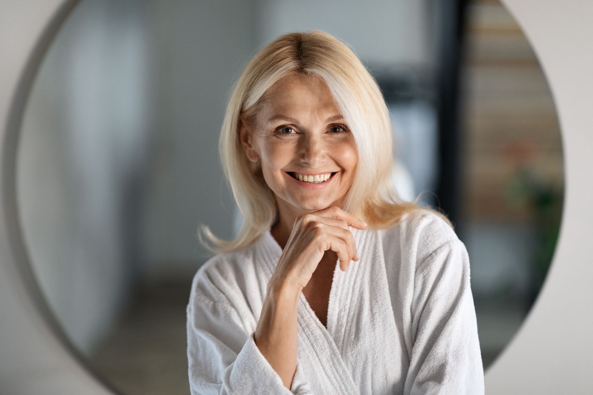 A woman in a bathrobe is smiling in front of a mirror.