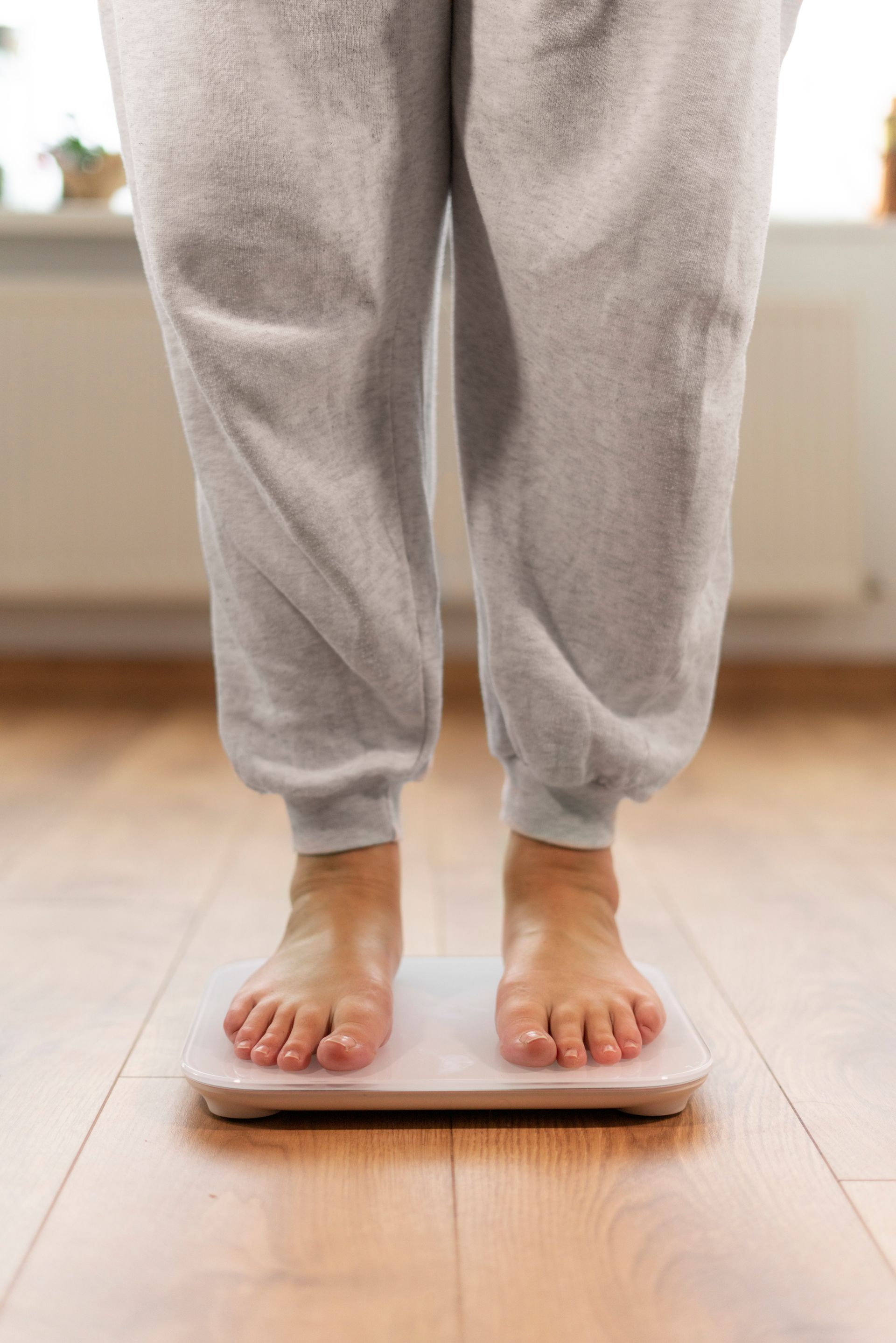 A person is standing on a scale on a wooden floor.