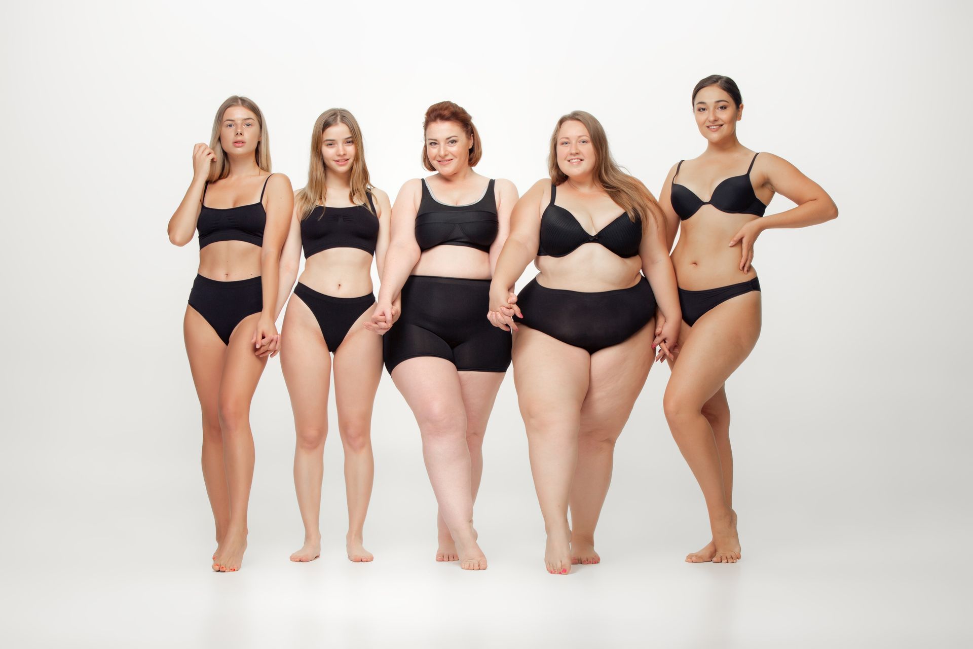 A group of plus size women in black underwear standing next to each other on a white background.