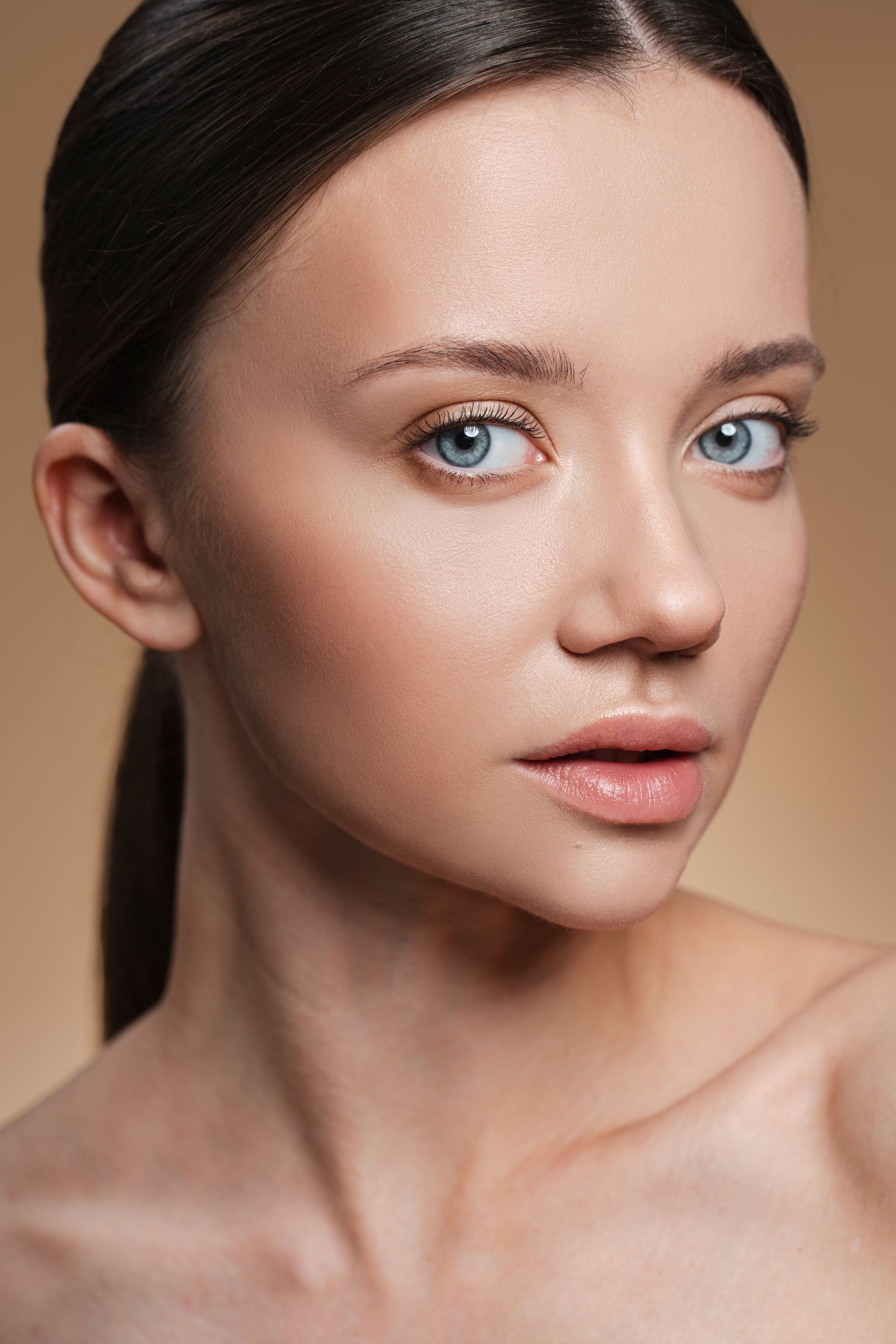 A close up of a woman 's face with a ponytail and blue eyes.