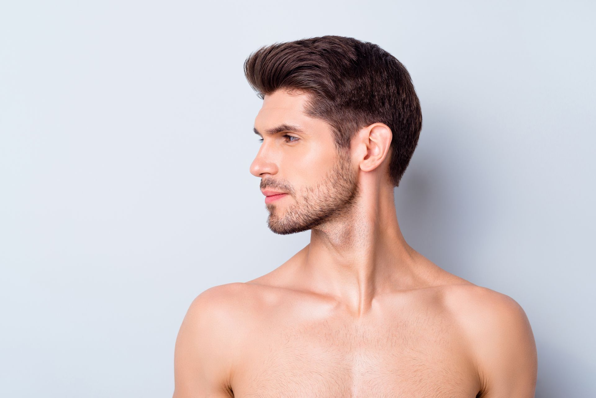 A shirtless man with a beard is looking to the side.