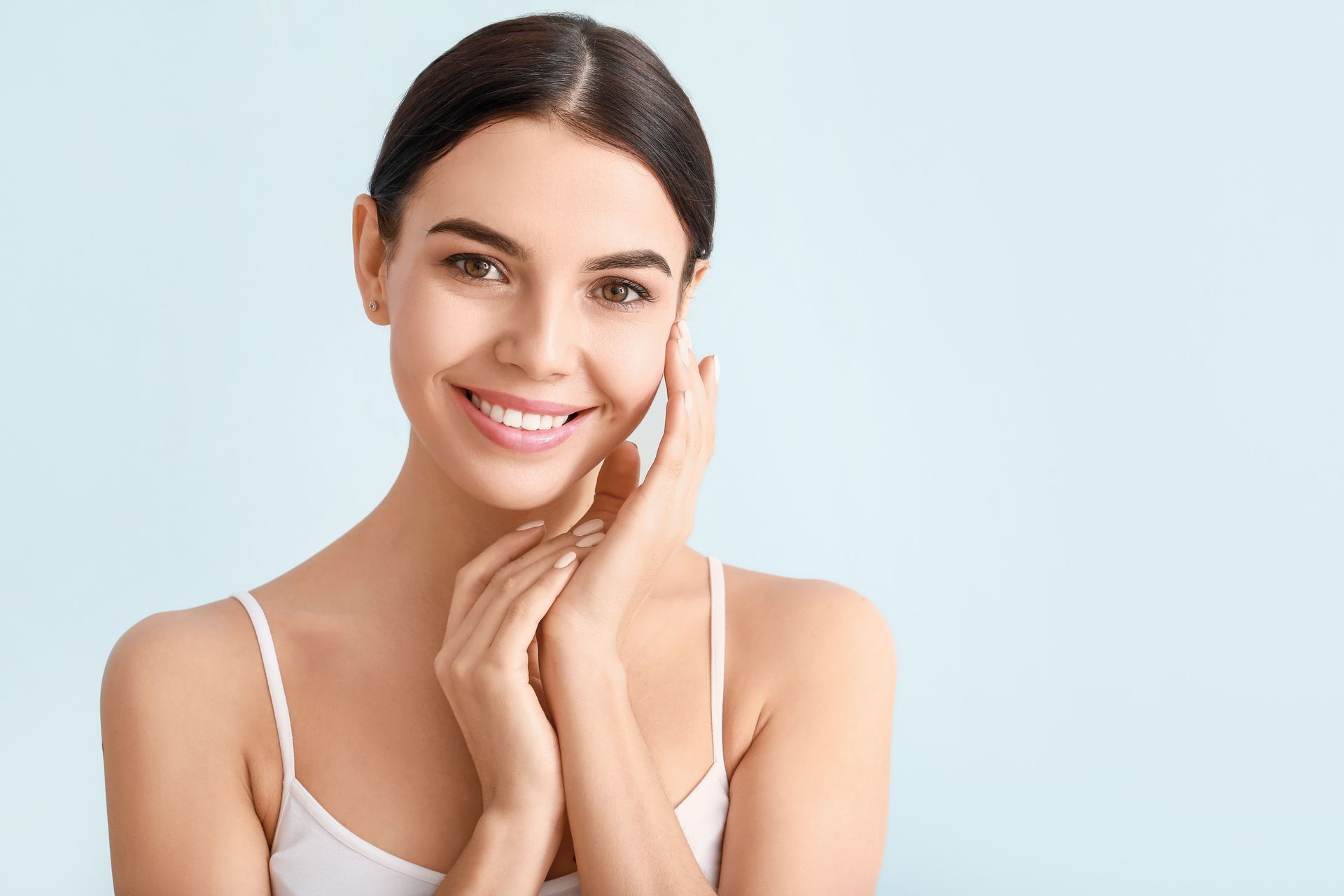 A woman is smiling and touching her face with her hands.