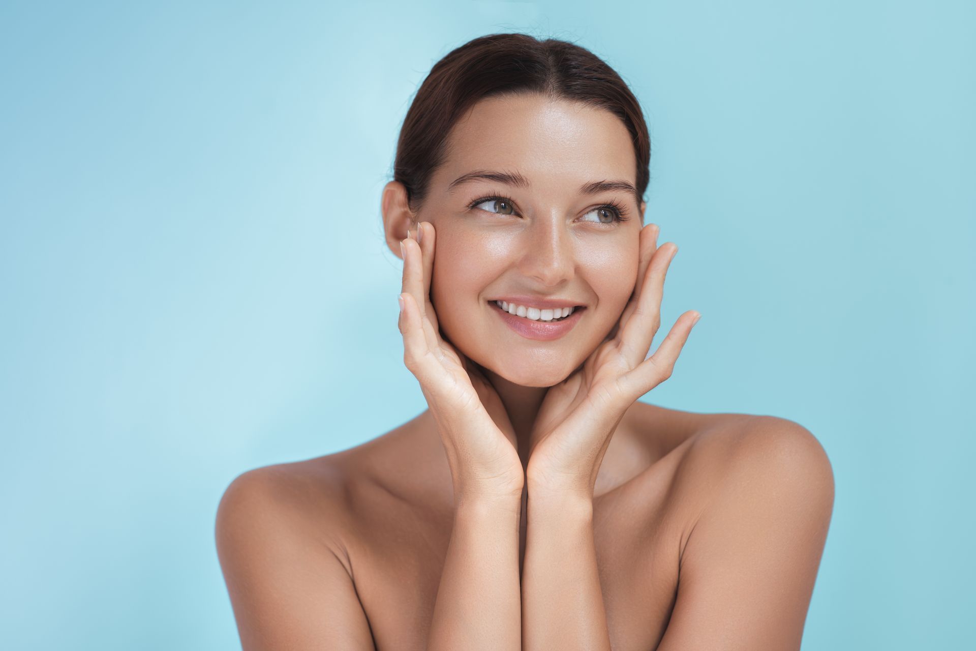 A woman is smiling and touching her face with her hands.