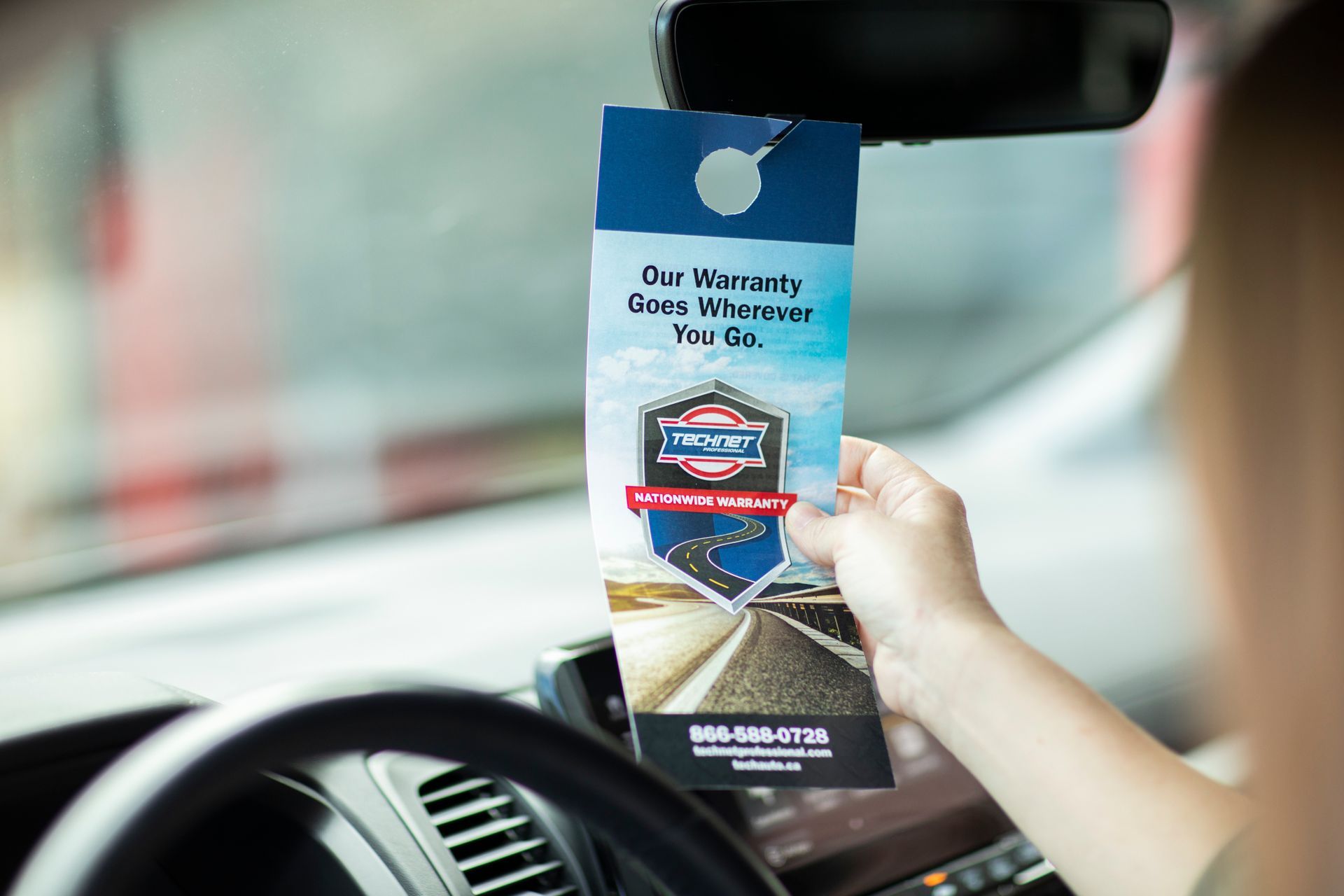 a person in a car holding a tag that says our warranty goes wherever you go