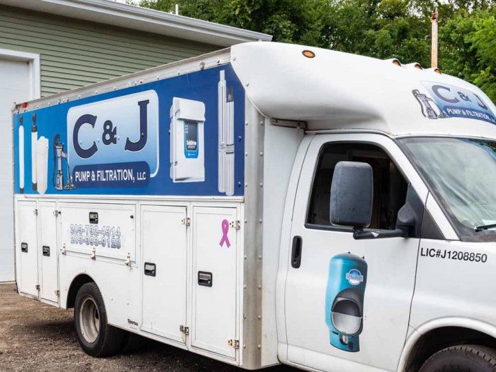 C&J plumbing service truck parked beside a house, with blue and white branding and pipe graphics