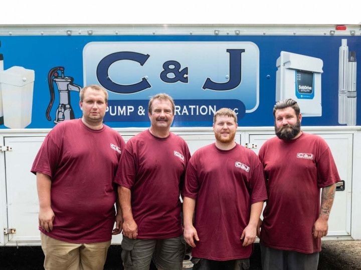 Four men in maroon shirts standing in front of a C&J Pump & Irrigation truck.