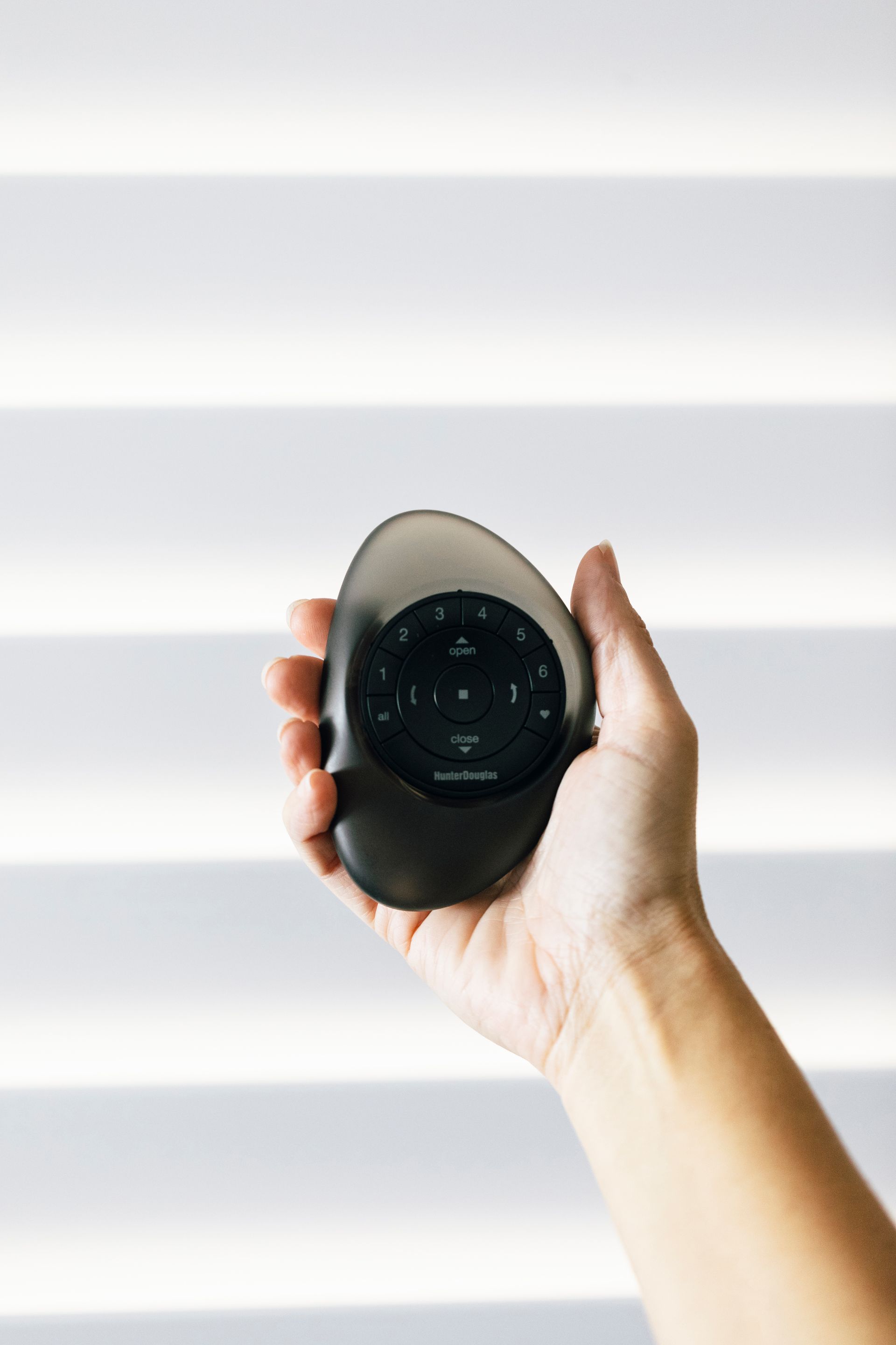 Hand holding a black oval device with a small screen against a bright white background