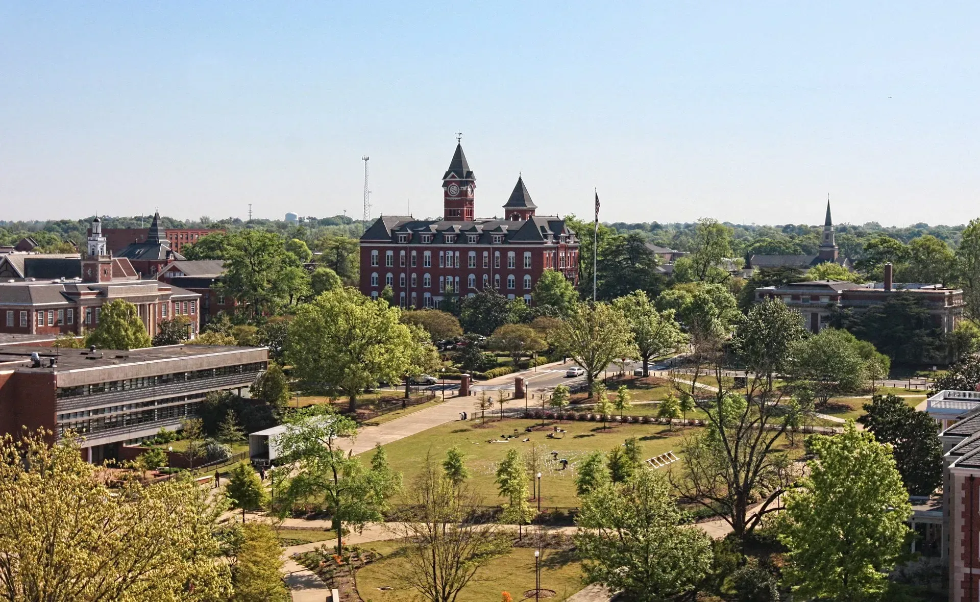 Wide city park with trees and paths, framed by historic red-brick buildings under a clear sky