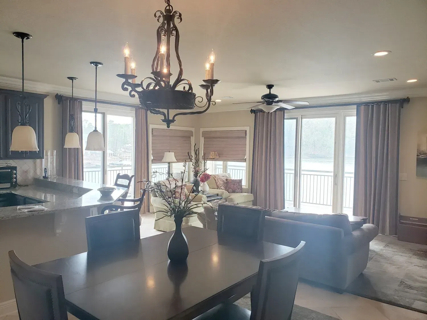 Open-concept living and dining room with dark furniture, chandelier, and large windows with curtains