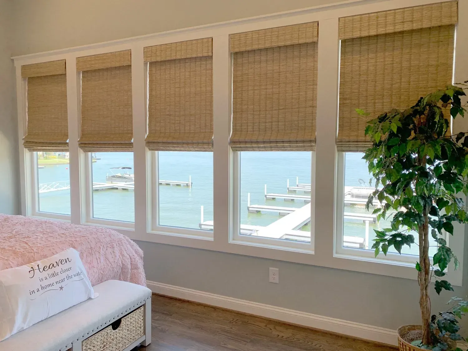 Bright room with large windows, woven shades, and a waterfront view with boats and trees