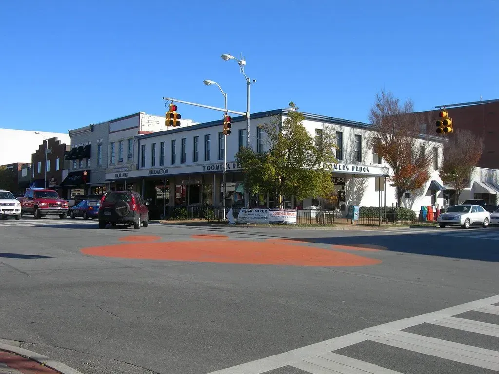 Urban street intersection with white buildings, cars, traffic lights, and a crosswalk on a sunny day