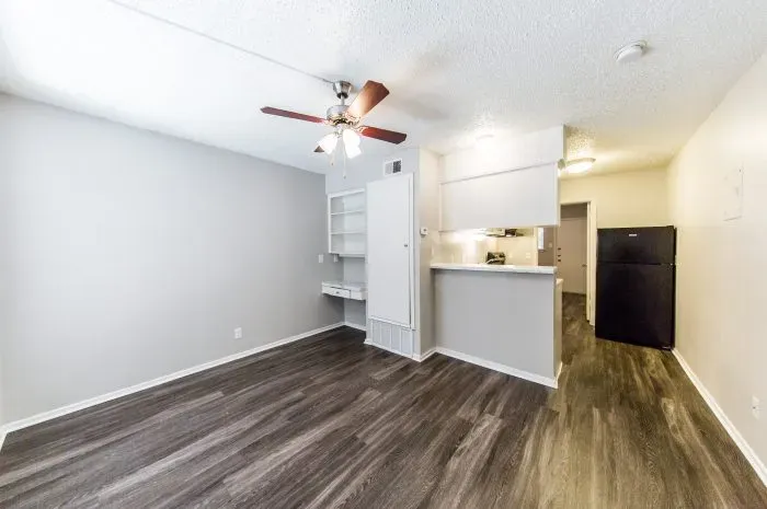 Pecan Square - living room with grey laminate flooring and ceiling fan looking into kitchen.
