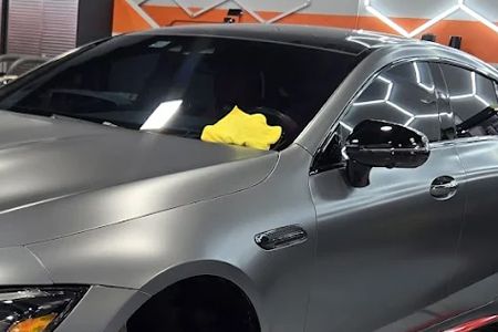 Gray sedan in a garage with a yellow cloth on the windshield near the passenger side.