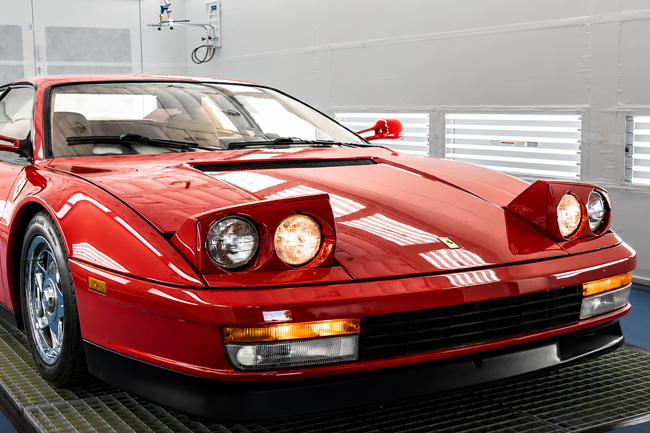 Red sports car in a garage, front view with pop-up headlights raised.