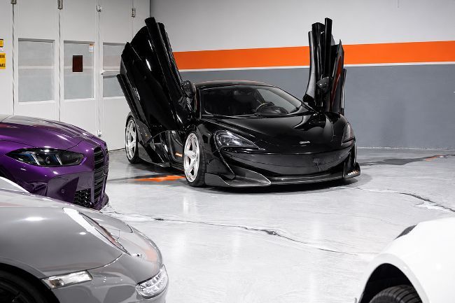 Black sports car with butterfly doors open in a garage, surrounded by other cars.
