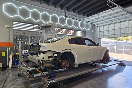 White sports car on a repair lift in an auto shop, with its rear disassembled and exposed.