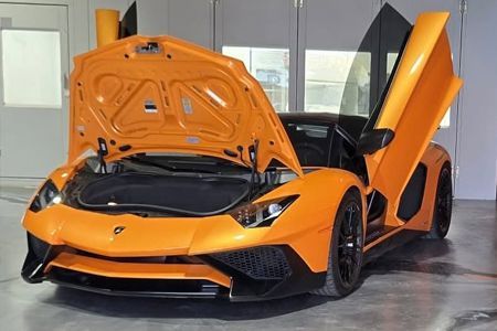 Orange Lamborghini with doors and hood open in a garage