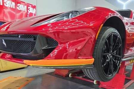 Red sports car on a lift in a workshop, front bumper and black wheel visible