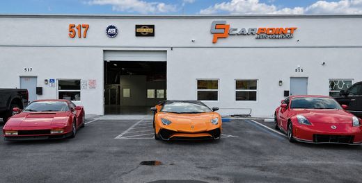 Three sports cars—red, orange, and red—parked outside an auto shop with open garage doors.