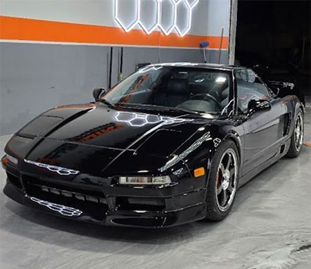 Black sports car parked indoors against a gray wall with orange stripe