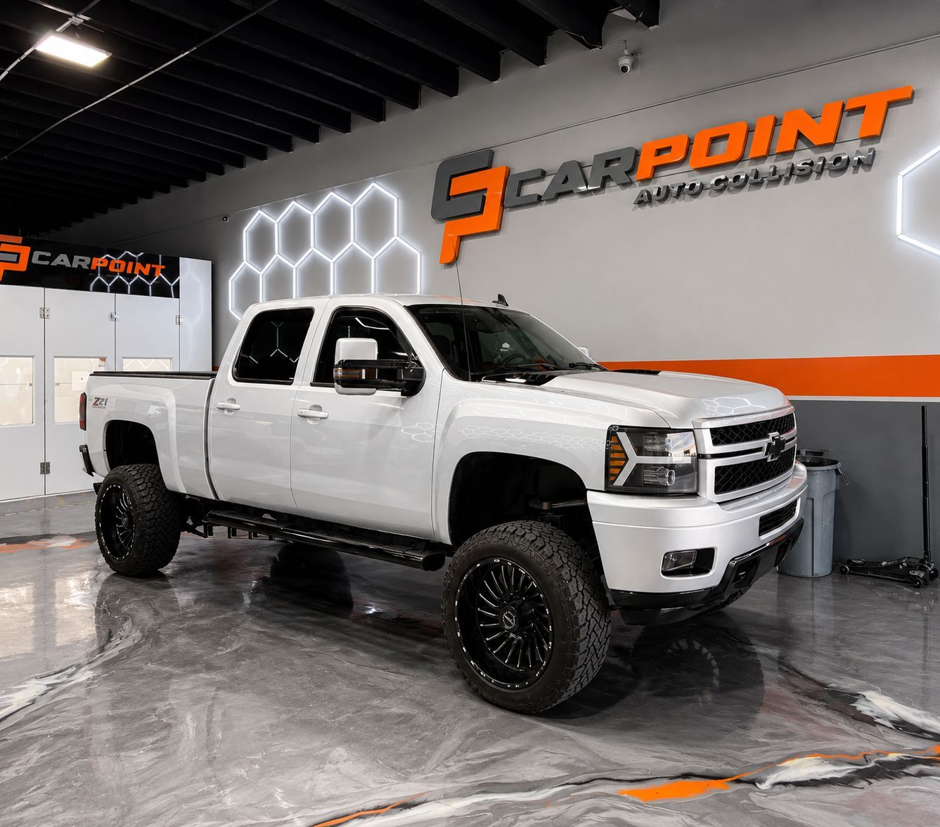 White lifted Chevrolet pickup truck in a car detailing showroom with CarPoint logo on the wall