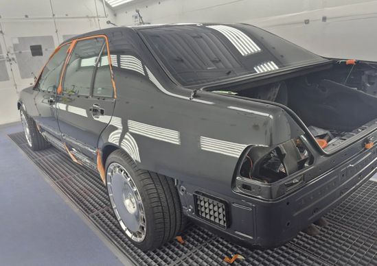 Black race car with open rear hatch, viewed in a garage on a blue floor