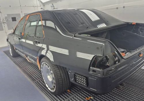 Black race car with open rear hatch, viewed in a garage on a blue floor