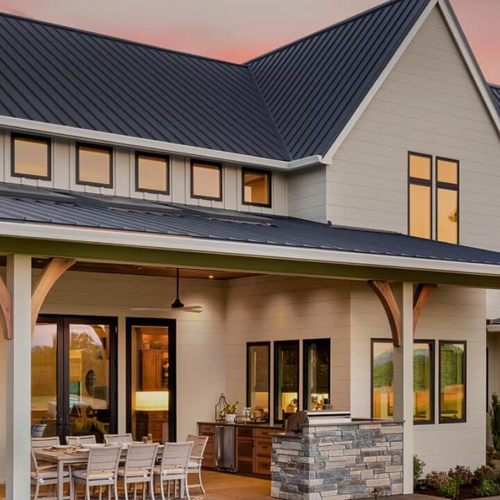 Modern house exterior with covered patio, dining table, stone accents, and warm sunset lighting