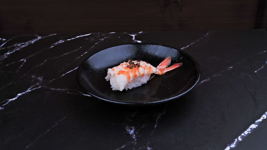 Nigiri sushi on a black plate, topped with green garnish on a dark marble table