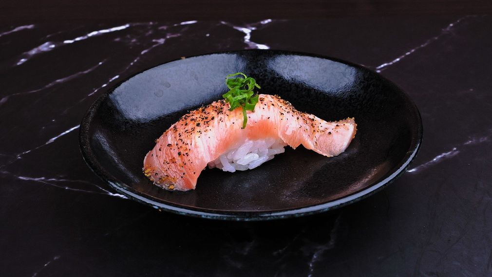 Salmon nigiri sushi on a black plate over a dark marble table