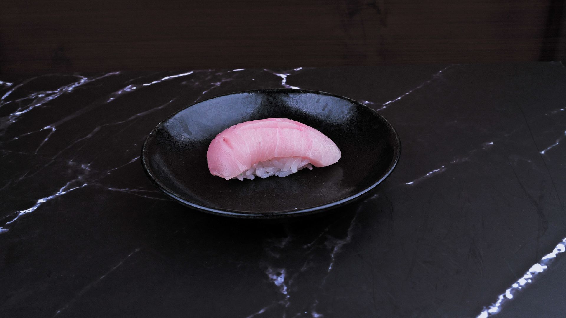 Pink sushi nigiri on a black plate atop a dark marble surface