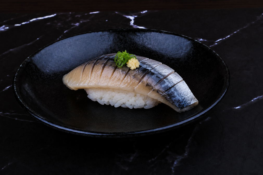 Nigiri sushi on a black plate, topped with green garnish on a dark marble table