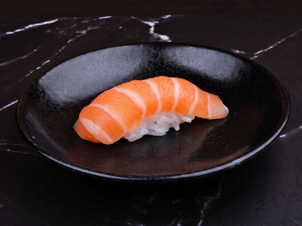 Salmon nigiri sushi on a black plate over a dark marble table