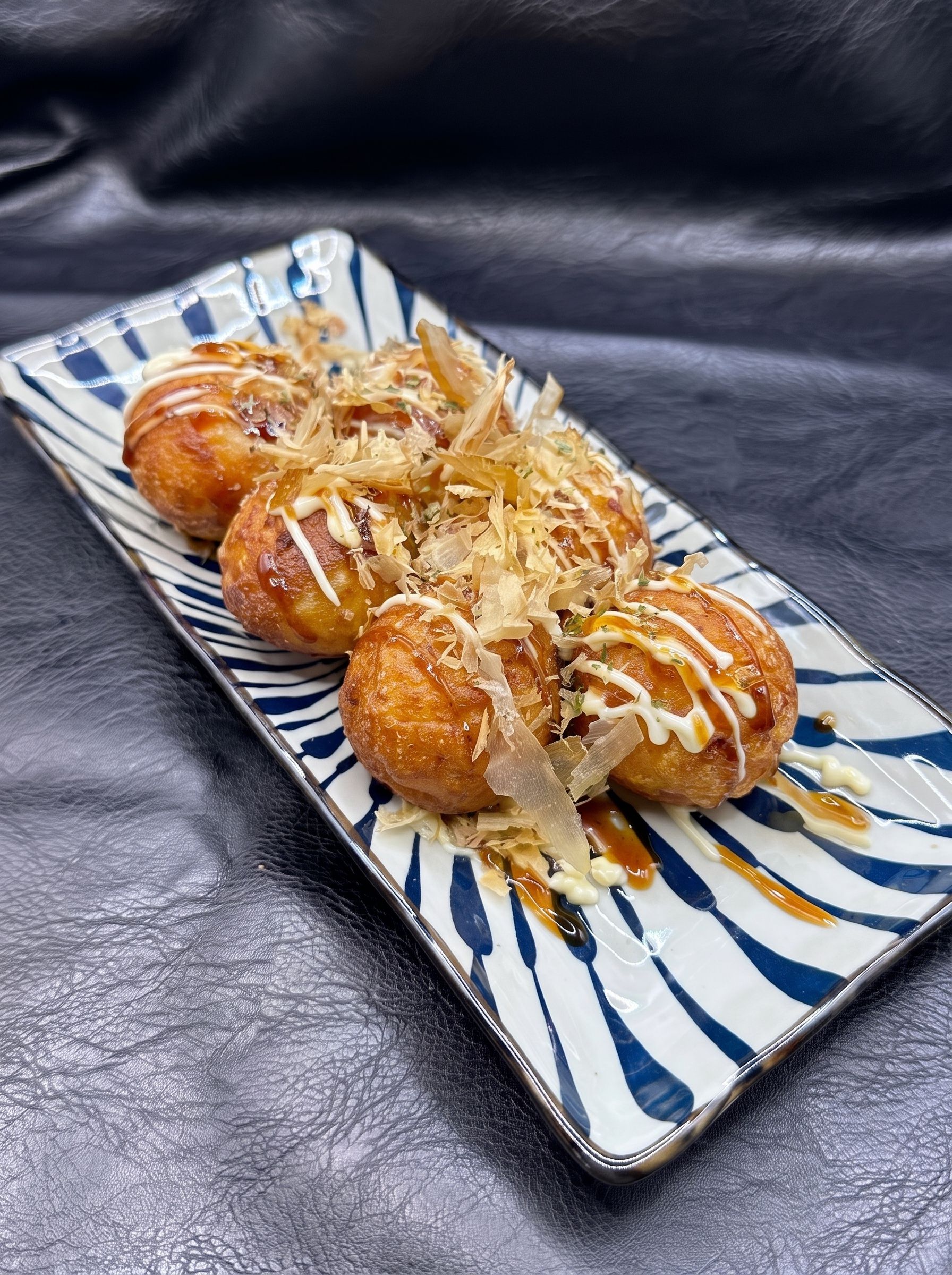 Four glazed pastries drizzled with white icing on a blue-and-white rectangular plate