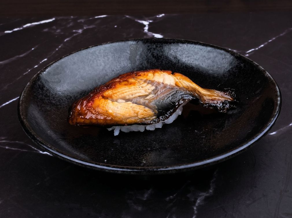 Grilled fish fillet on a black plate, served on a dark table.