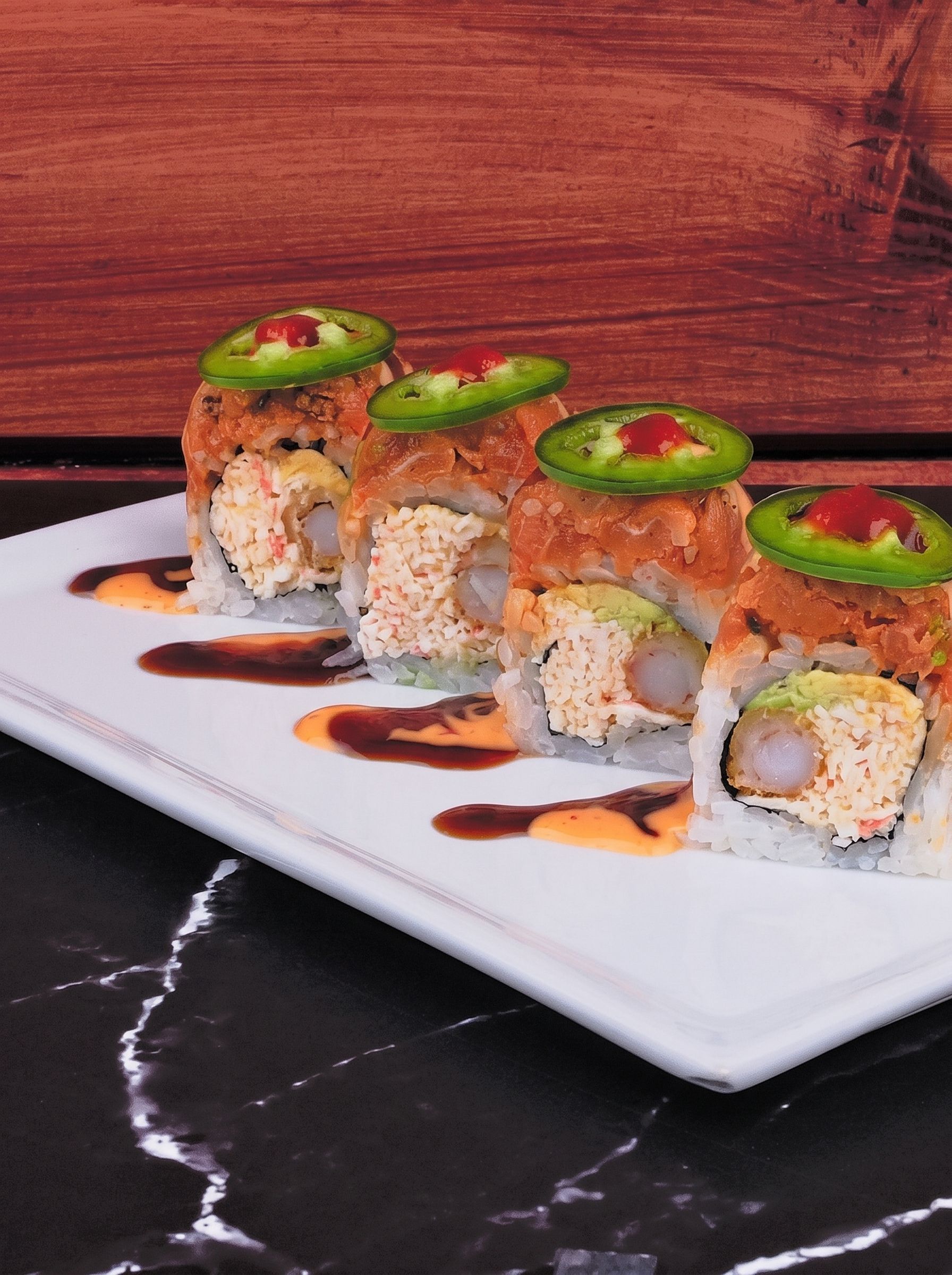 Sushi rolls topped with avocado and red garnish, arranged on a white plate with sauce drizzles.