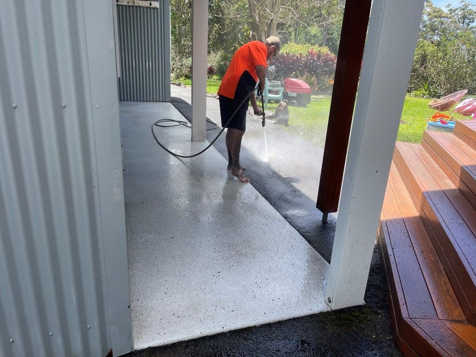 A Man is Using a High Pressure Washer to Clean a Concrete Floor — Goat Collective in Tintenbar, NSW
