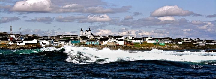 Coastal town with houses and a church by rough blue water under cloudy skies
