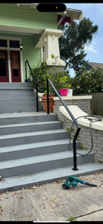 Front porch staircase with black railing, green house siding, and a teal drill on the driveway below.