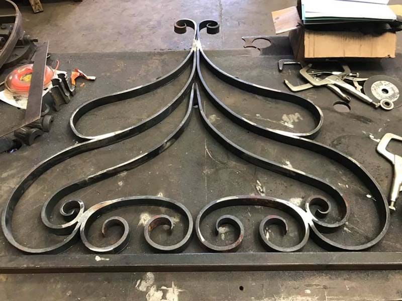 Black wrought-iron decorative gate panel with scrollwork on a workbench