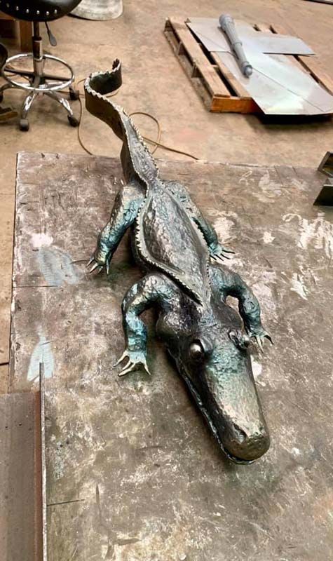 A crocodile lies on a concrete floor beside a chair and wooden boards.