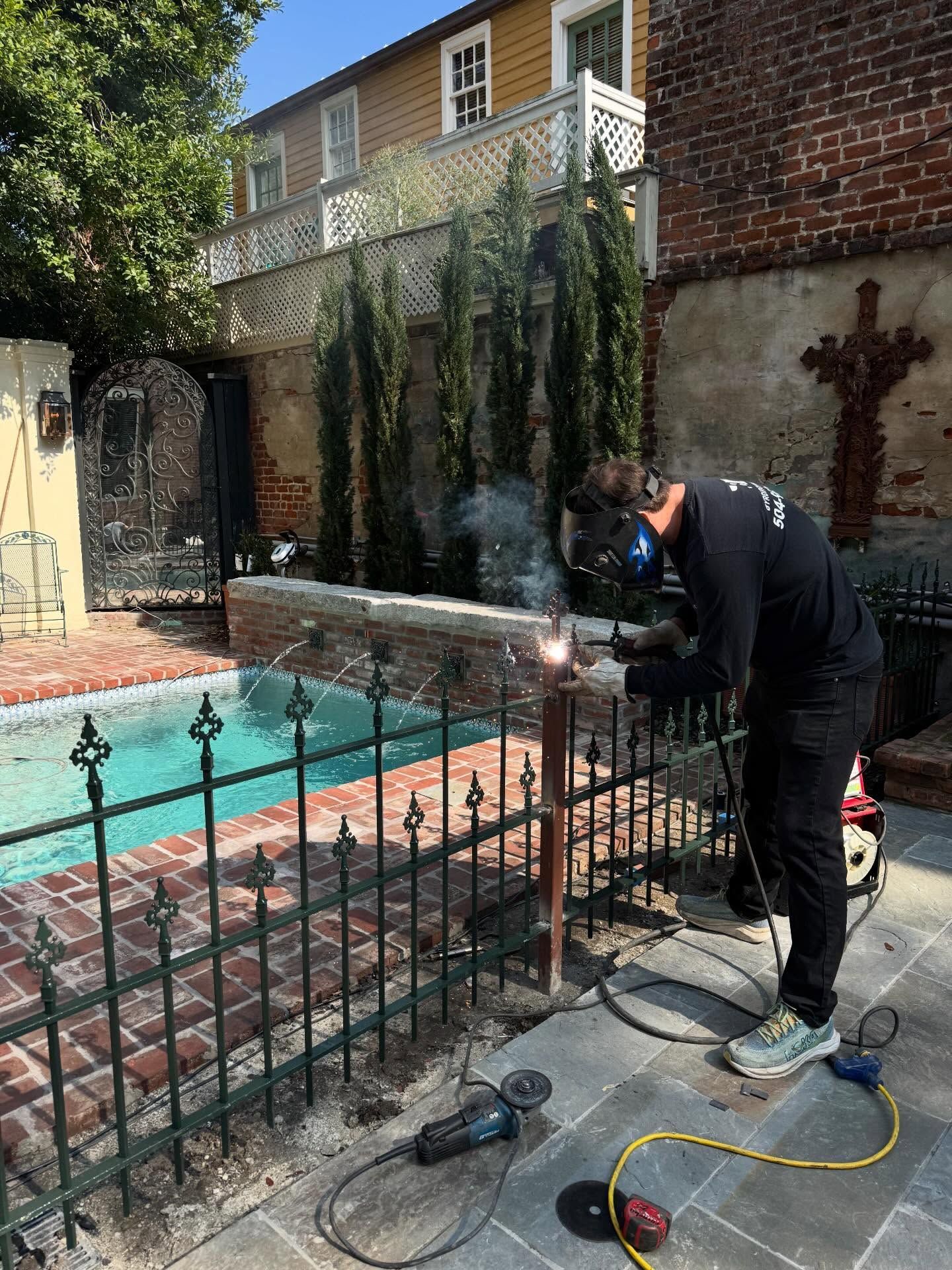 Person using a pressure washer beside a pool in a brick courtyard