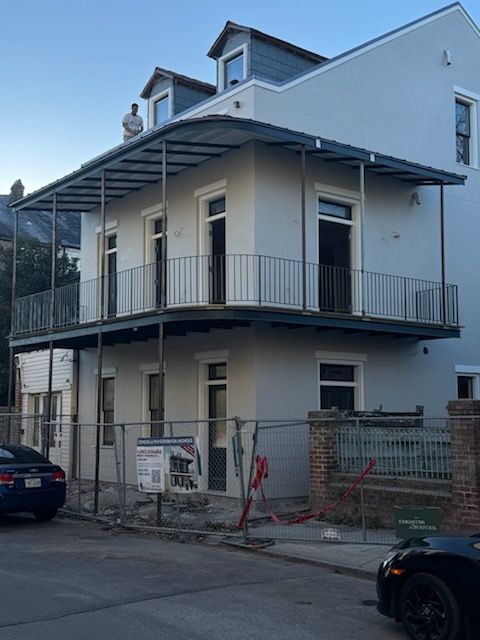 Two-story white house with a wraparound porch and metal railing, viewed from the street