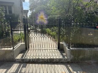 Wrought-iron gate opening to a sunlit garden path with low stone walls and a house in the background