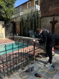 Worker using a tool near a pool beside a wrought-iron fence and brick patio