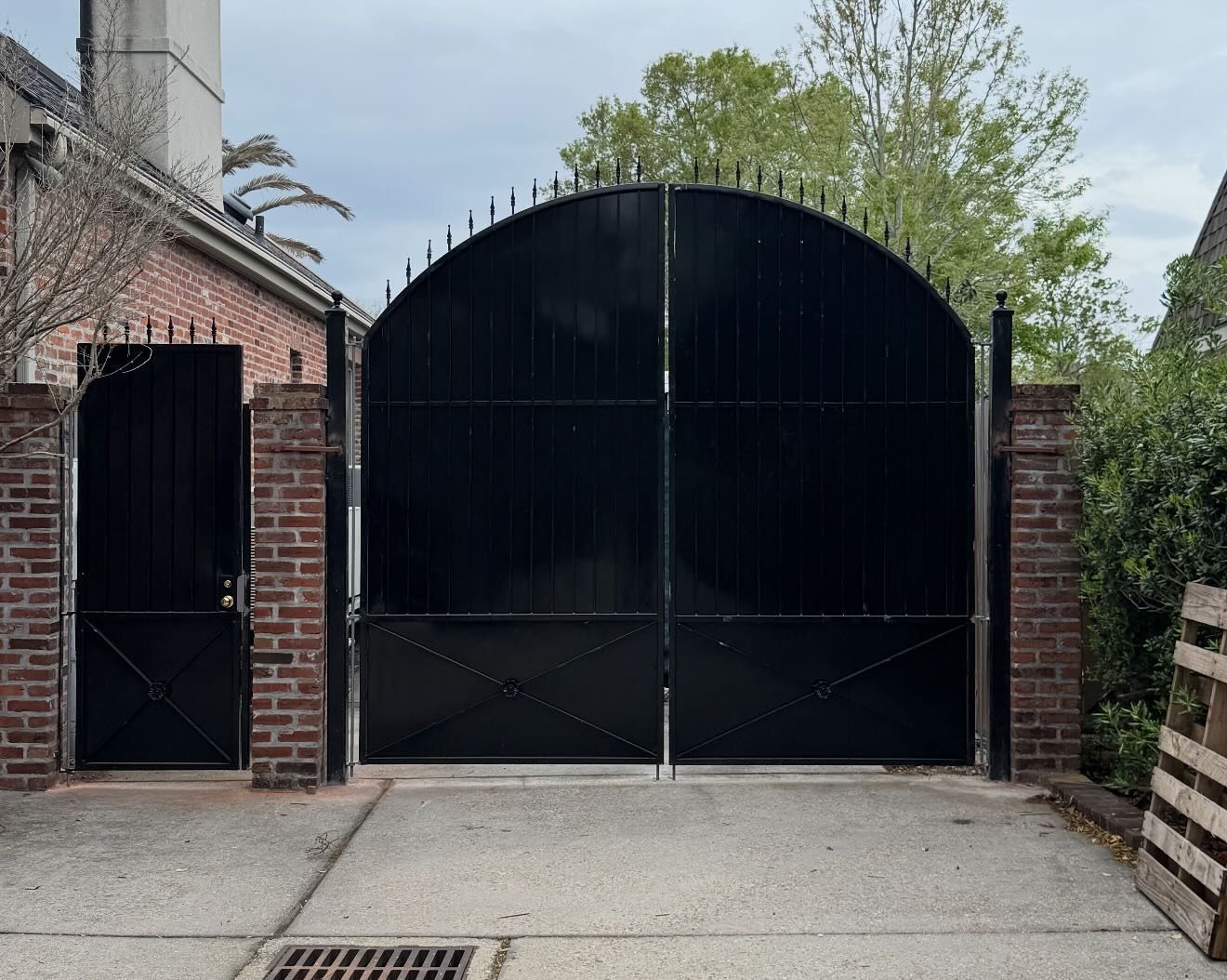 Black arched metal gate between brick pillars in a driveway beside a brick building