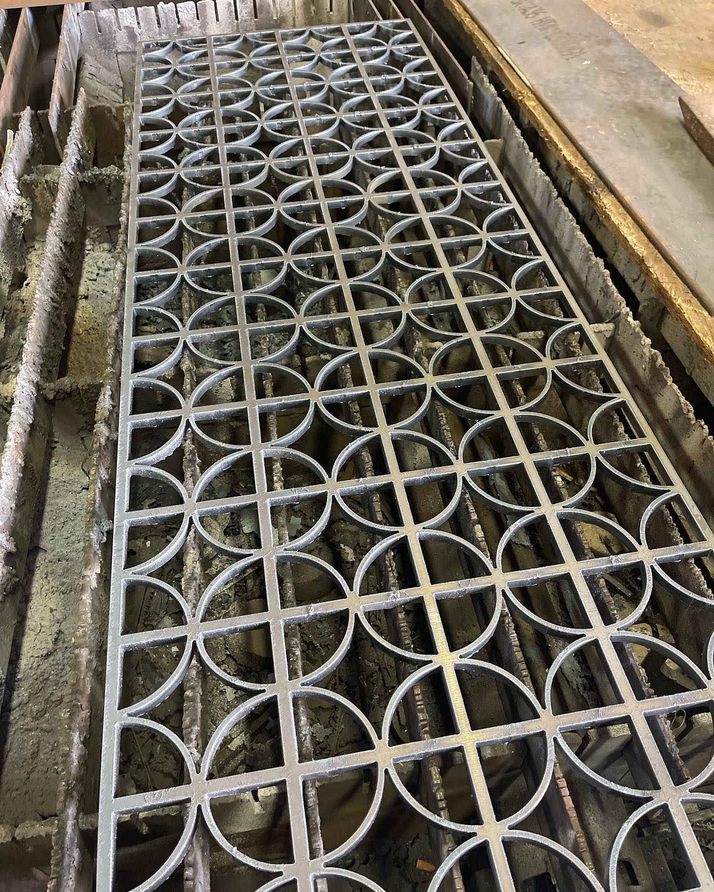 Metal decorative grate with repeating circular lattice pattern on a concrete surface